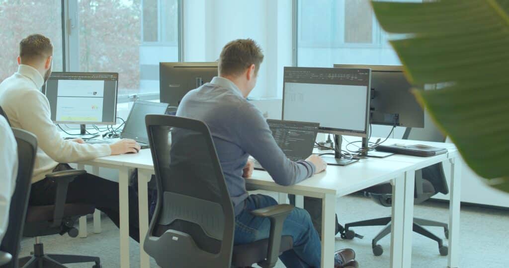 Twee mannen zitten aan een bureau te werken op hun laptop